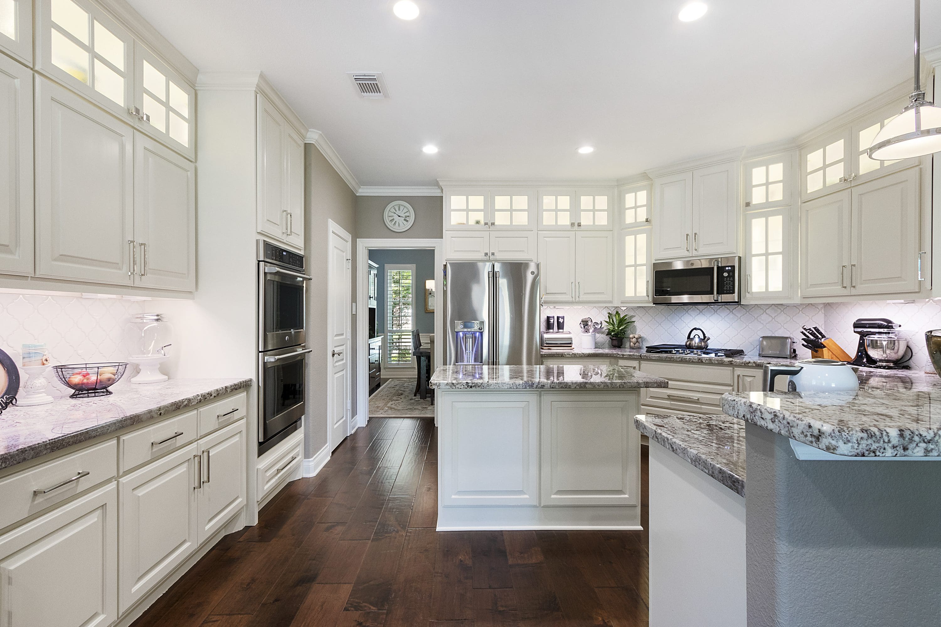 A kitchen with white cabinets and wood floors.