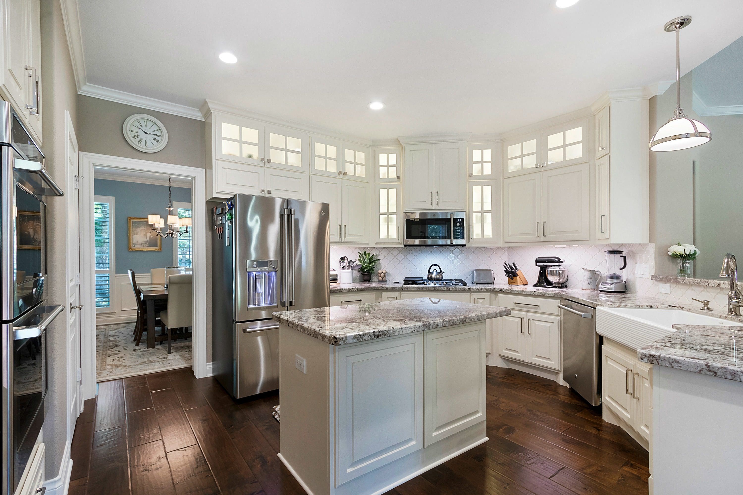 A kitchen with white cabinets and wood floors.