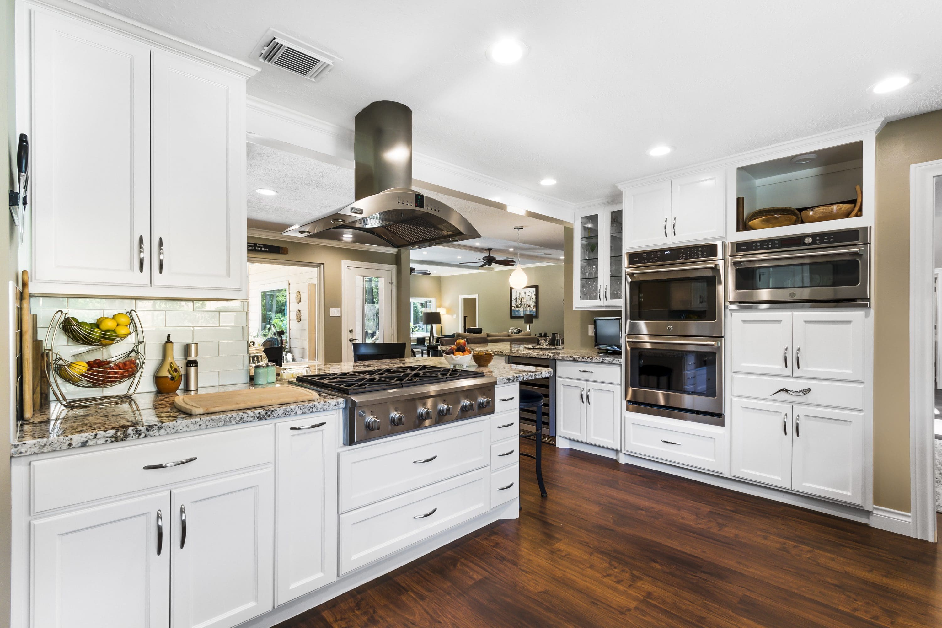 A kitchen with white cabinets and wood floors.