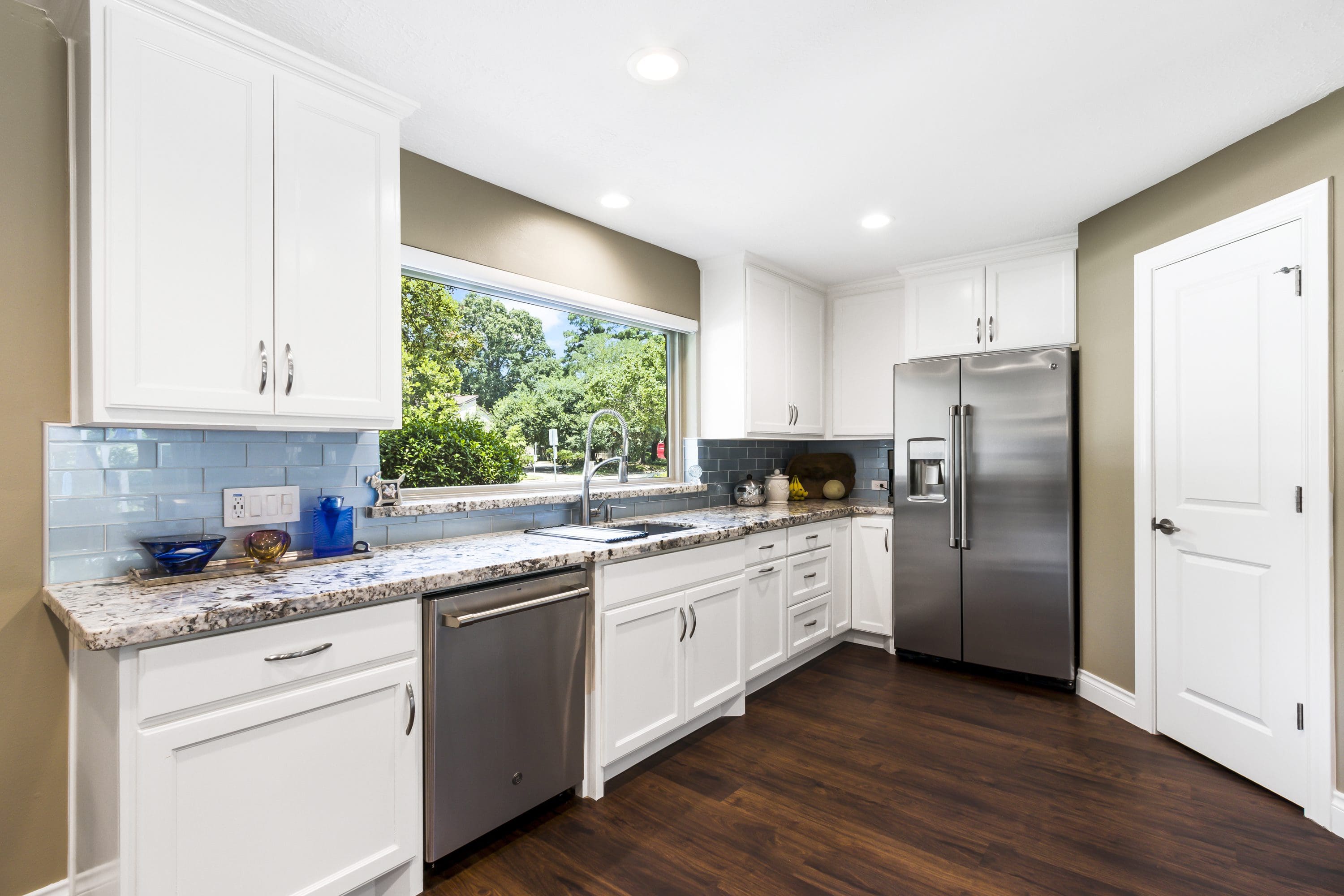 A kitchen with white cabinets and wood floors.