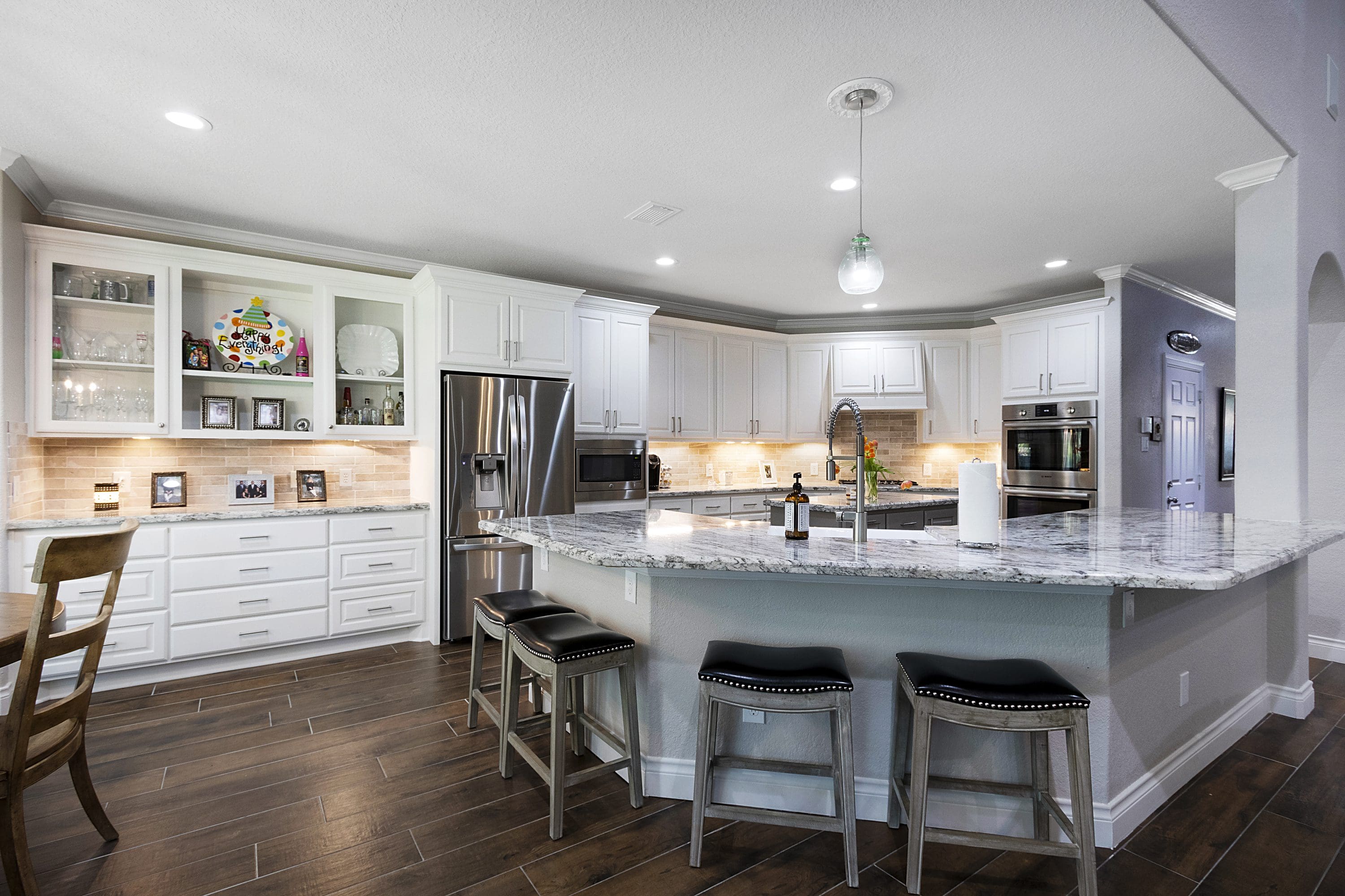A kitchen with white cabinets and black stools.