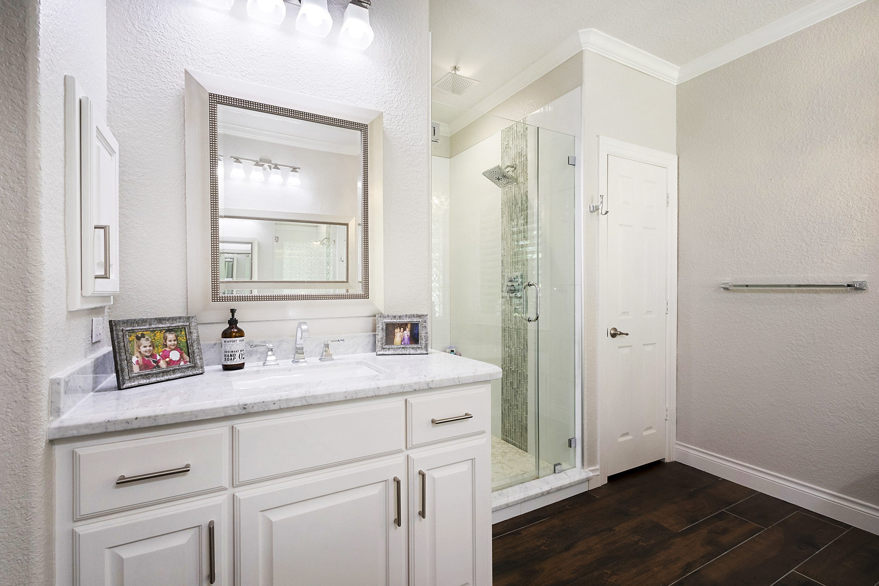 A bathroom with white cabinets and a glass shower door.