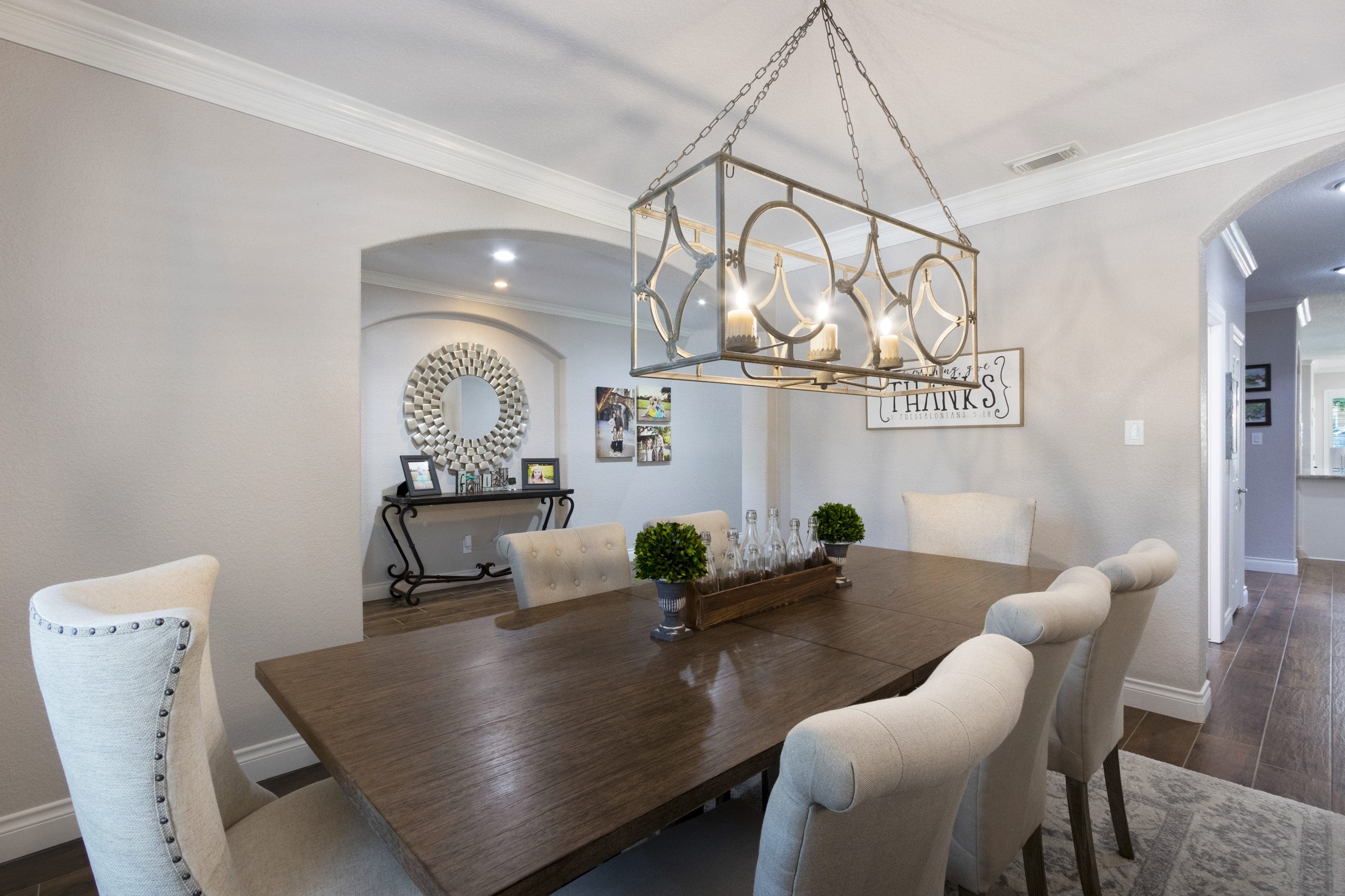 A dining room table with white chairs and a chandelier.