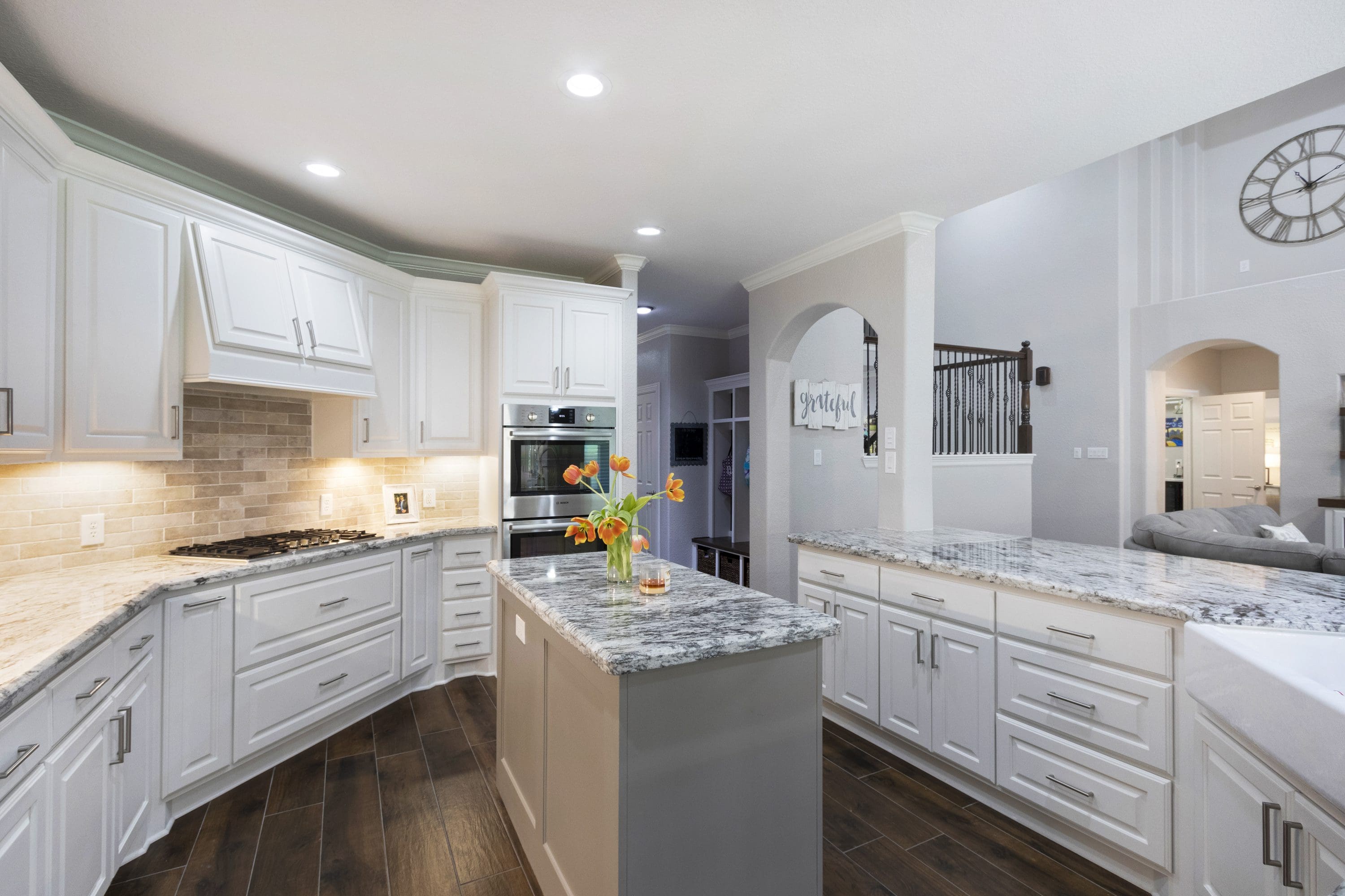 A kitchen with white cabinets and wood floors.