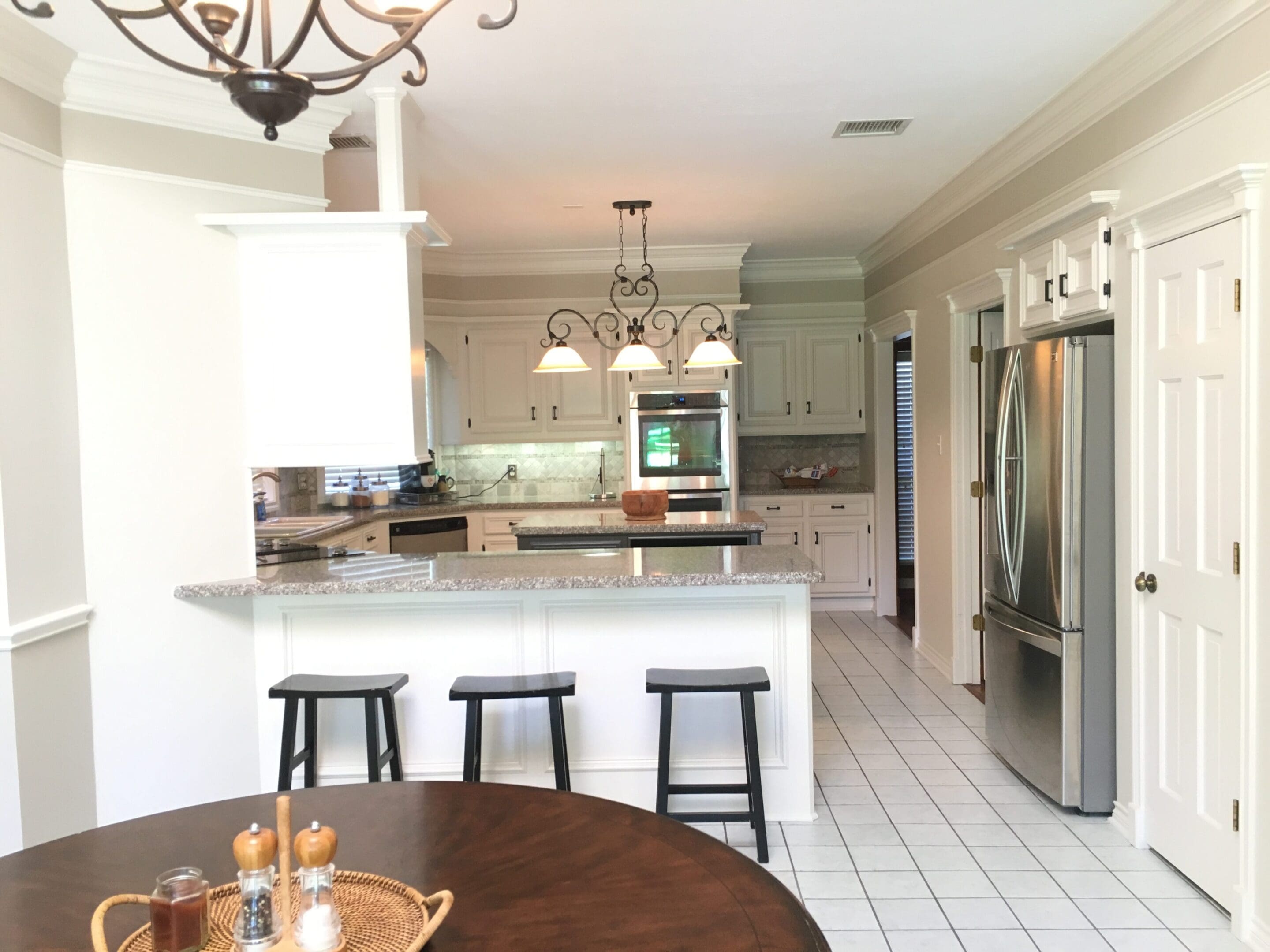 A kitchen with white cabinets and black stools.