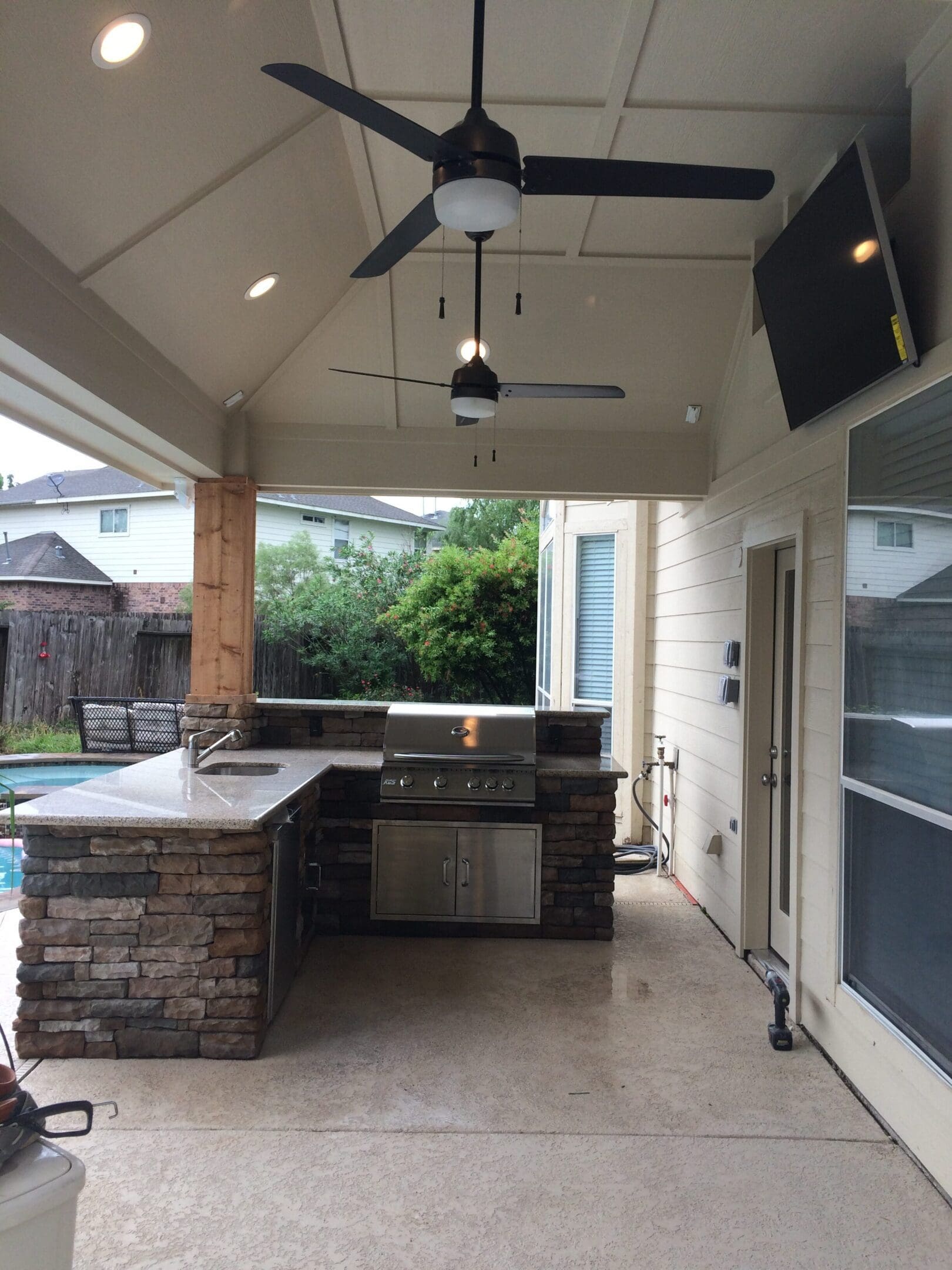 A covered patio with an outdoor kitchen and television.