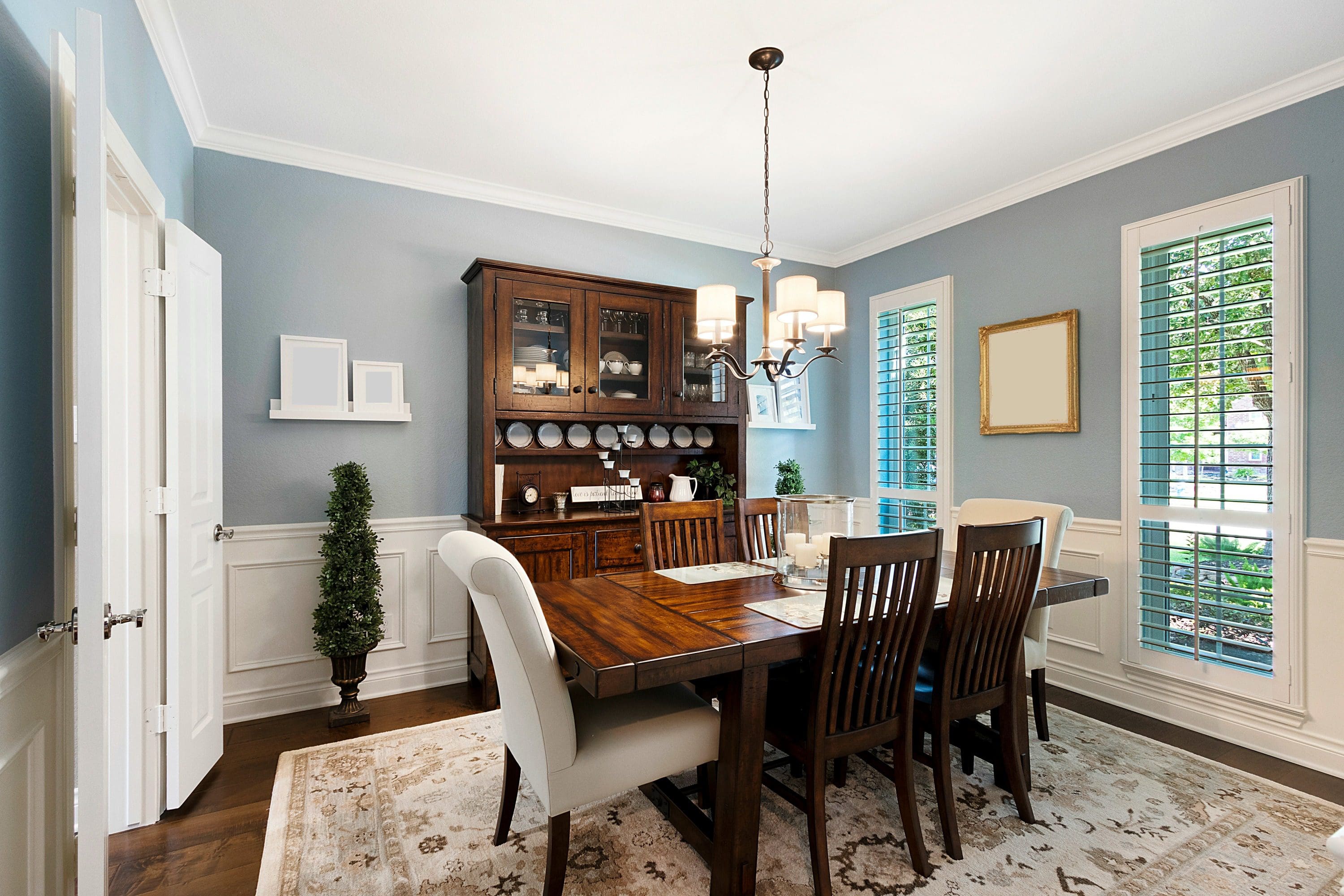 Blog#2 Thimbnail A dining room with a table and chairs, a china cabinet and a plant.